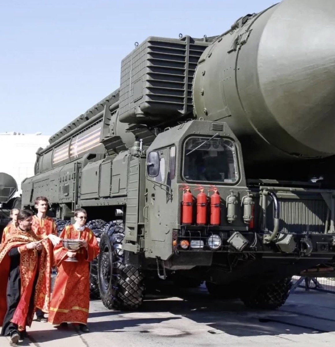 Russian Orthodox priests walking alongside RS-24 Yars intercontinental ballistic missile launchers with holy water at Khodynka Field, Moscow