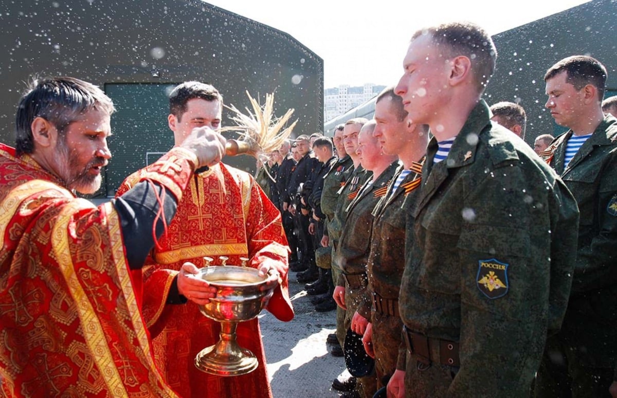 Russian servicemen wearing St. George's ribbons being blessed with holy water by a priest on Victory Day