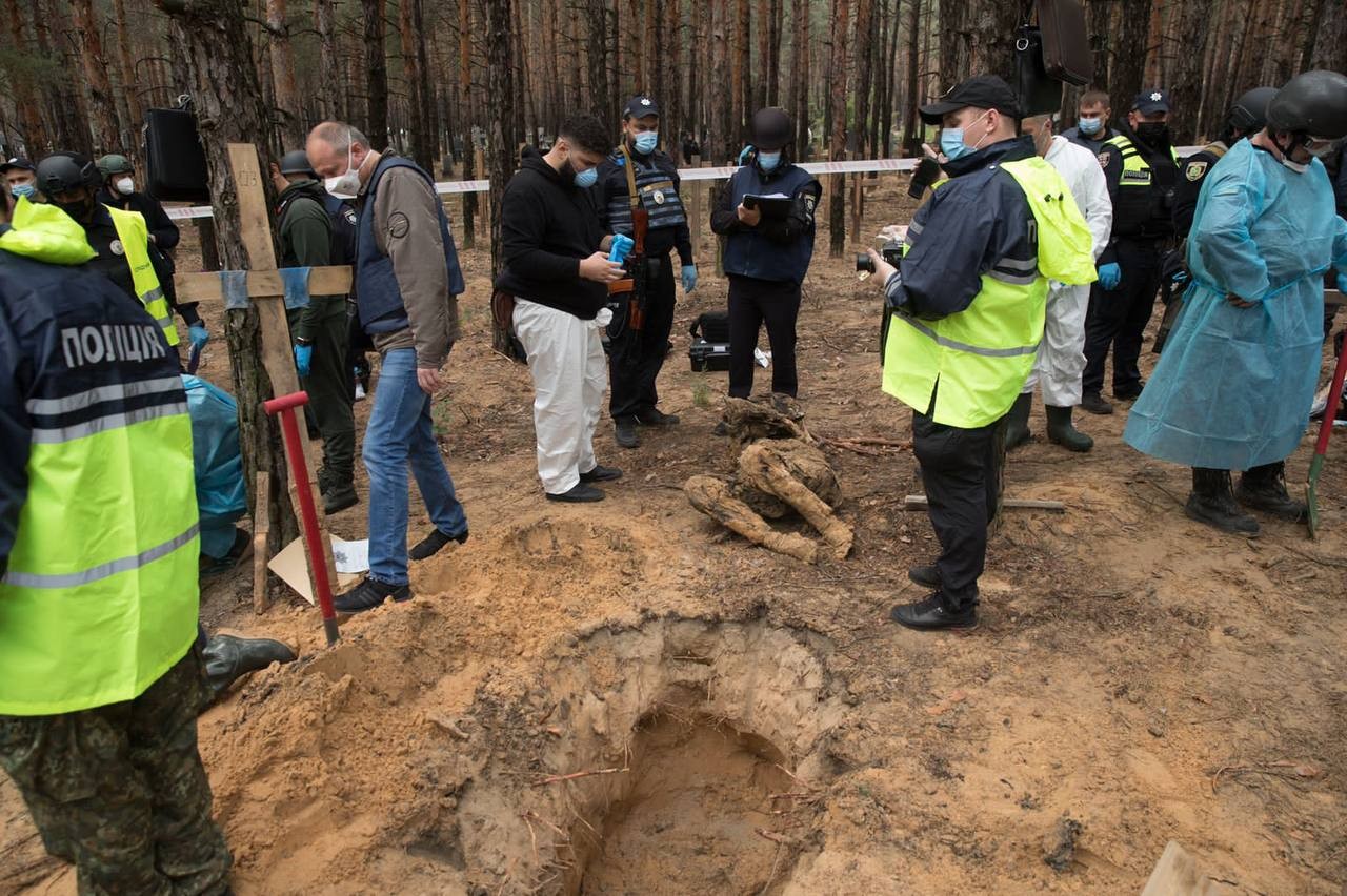 Mass graves in Izium, rows of wooden crosses marking individual graves in a forest clearing