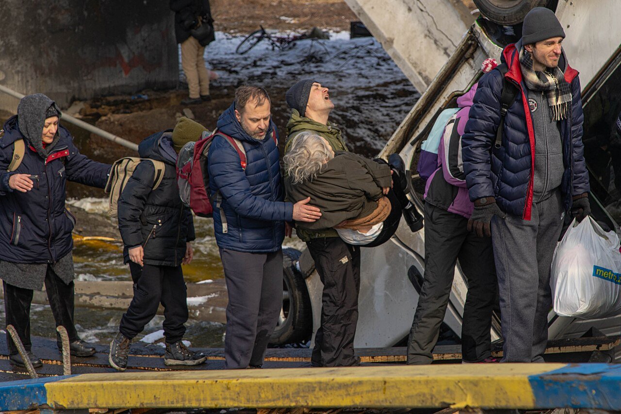 Civilians evacuating across the destroyed bridge in Irpin, a man carrying an elderly woman