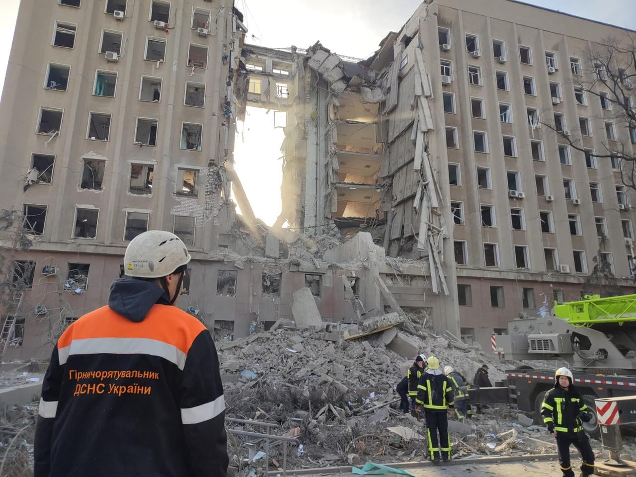 Mykolaiv Regional Administration building with center section destroyed, emergency workers in foreground