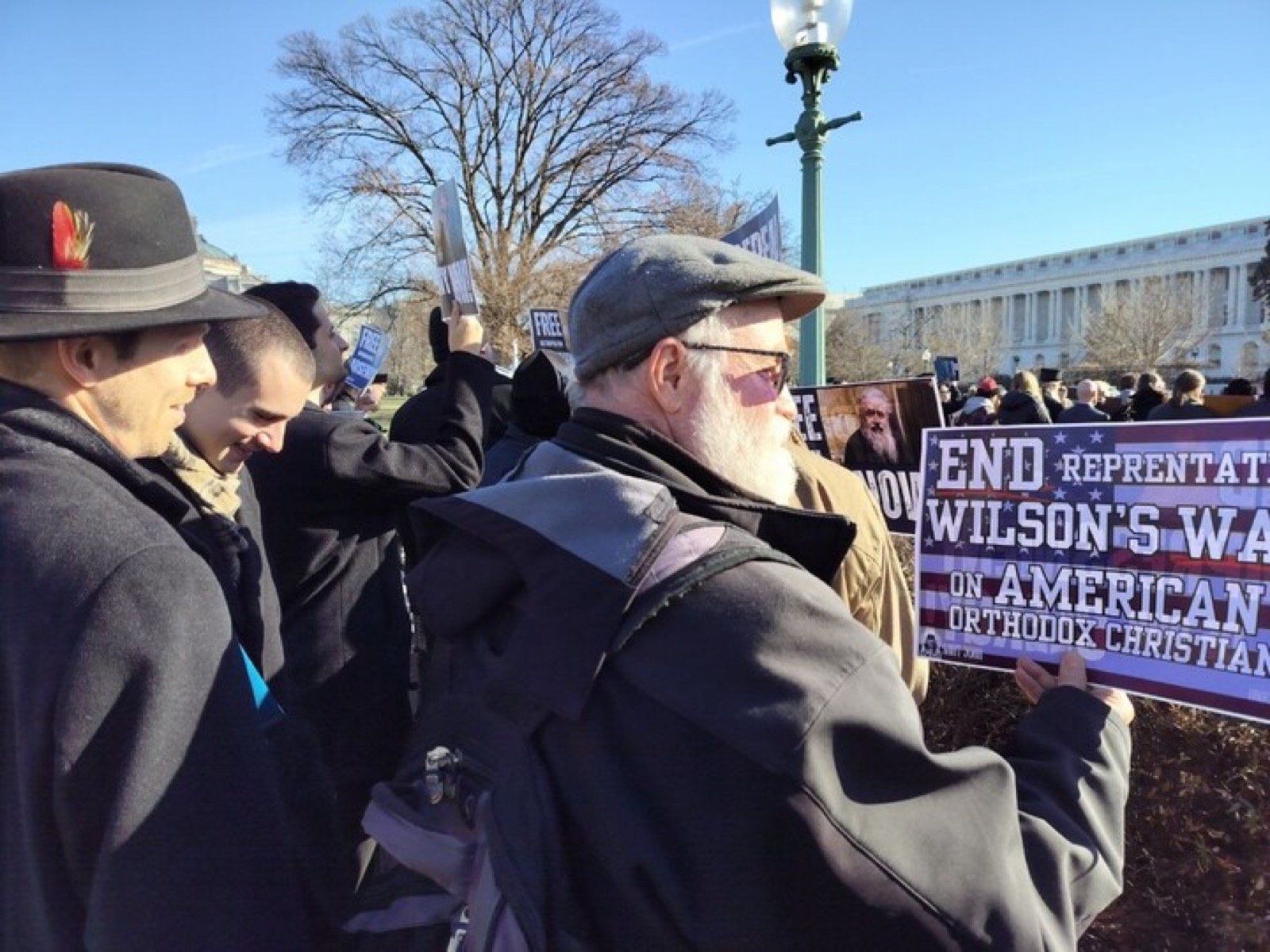 A delegate holds a sign reading "END Representative Wilson's War on American Orthodox Christians."
