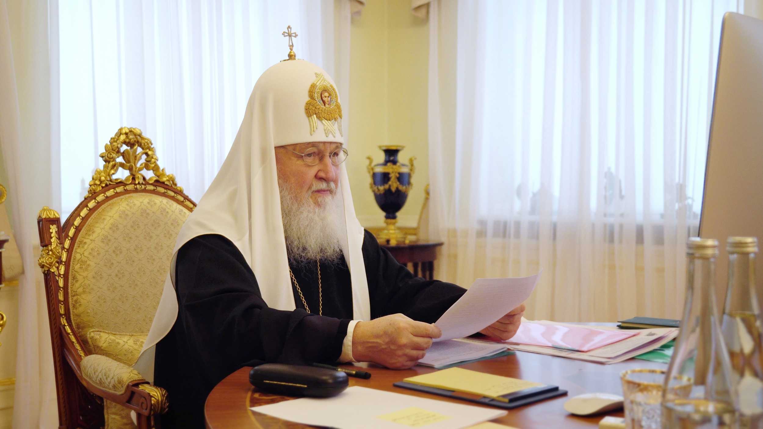 Patriarch Kirill seated at his desk in white klobuk, reading from papers during the Moscow Diocesan Assembly conducted via Zoom