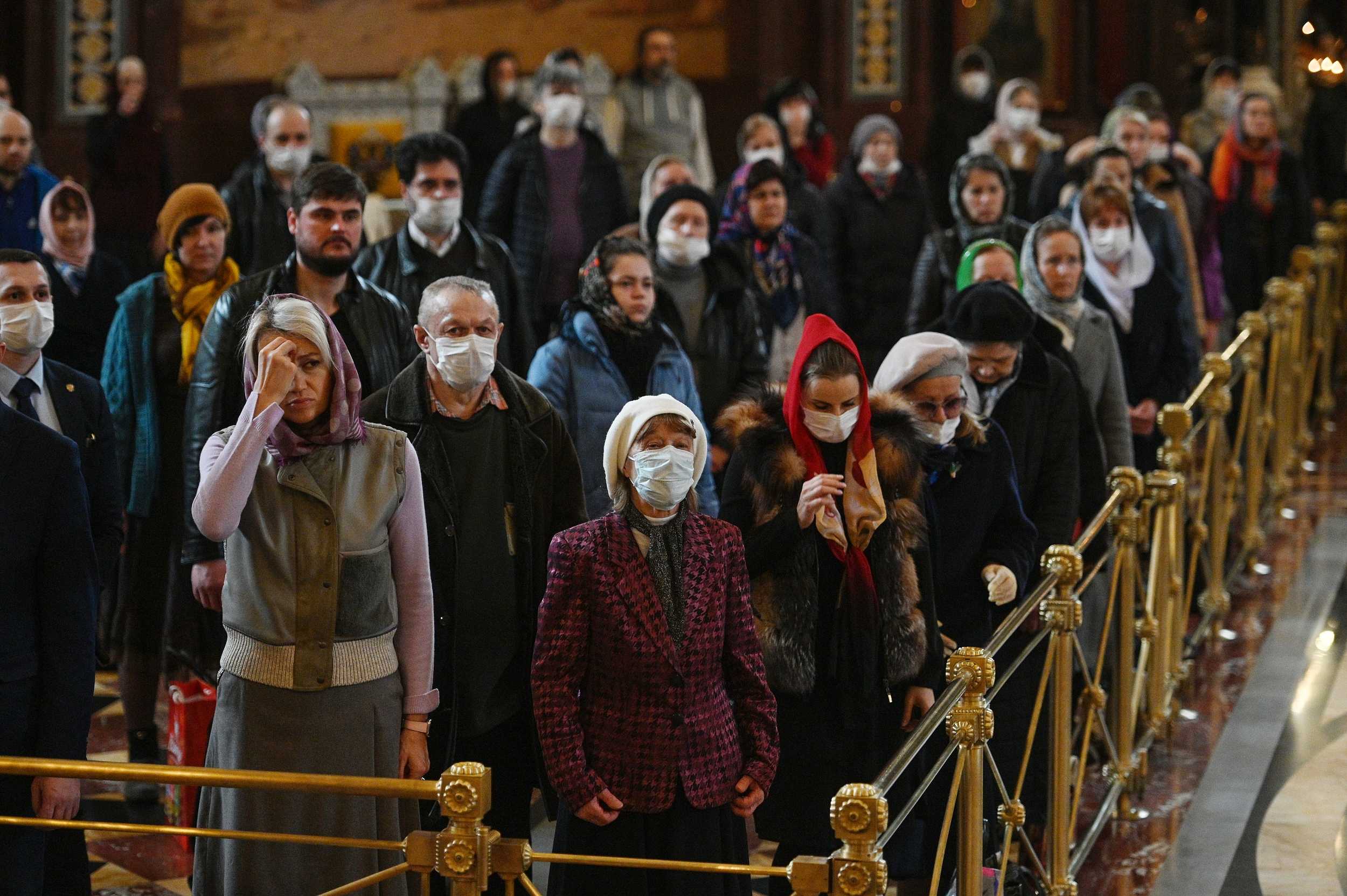 Faithful standing behind gold barriers at the Cathedral of Christ the Saviour during a COVID-era service, many wearing medical masks